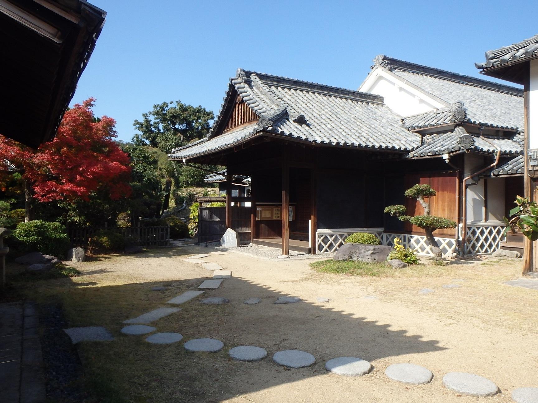 雲一つない晴天の下建つ瓦屋根の林求馬邸を玄関へと続く白色の飛び石側から撮影した写真