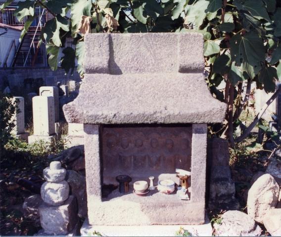 石造りの小さな祠の中収められた石像の六地蔵の前に供えられた湯飲みに入った飲み物や線香の写真
