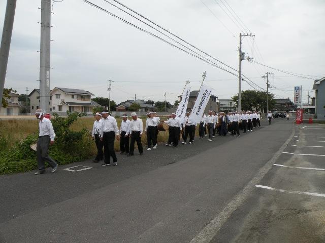 大般若波羅蜜多経を長持ちに入れのぼり旗を掲げながら縦に整列し道路を歩く南鴨の大般若経巡行をおこなう人々の写真