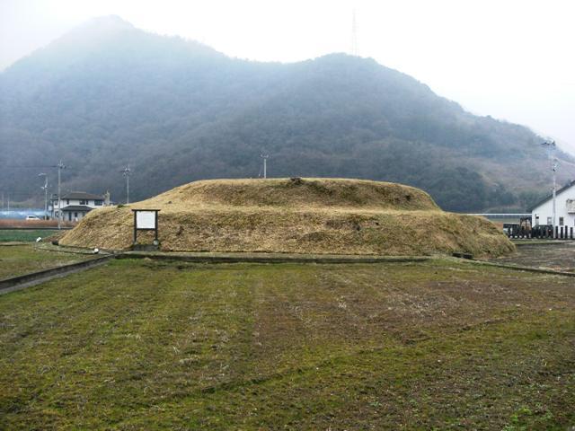 天霧山を背景に2段の墳丘2重の周濠を持つ多度津町奥白方最大級の盛土山古墳をやや遠目のアングルから撮影した写真