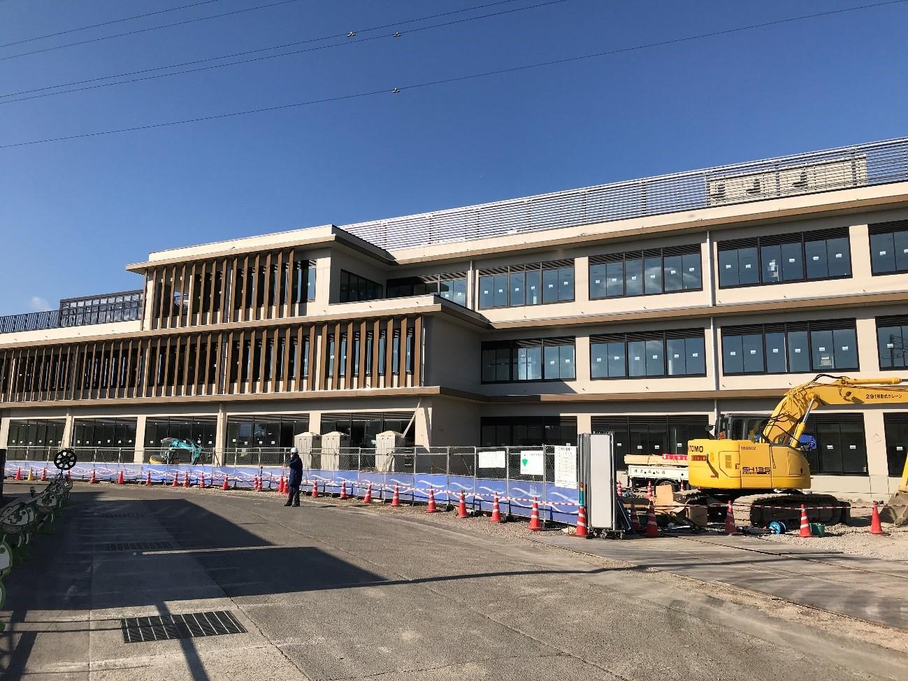 黄色や緑色のショベルカーを使用した多度津町新庁舎工事の東面外装の様子を青空の下12月20日に撮影した写真